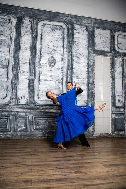 młody mężczyzna tańczy z dziewczyną w niebieskiej sukni balowej w szarej sali tanecznej - Zdjęcie, obraz