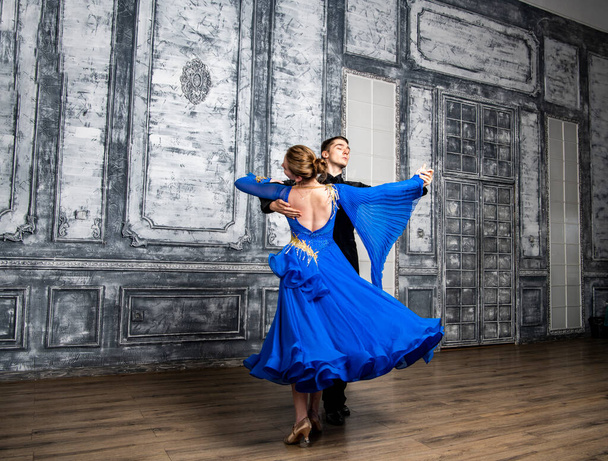 Genç adam, gri dans salonunda mavi balo elbiseli bir kızla dans ediyor. - Fotoğraf, Görsel