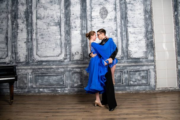 joven bailando con una chica en un vestido de salón azul en un salón de baile gris - Foto, imagen
