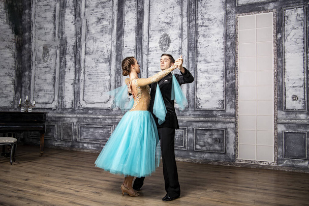 un giovane uomo in abito nero sta ballando con una ragazza in abito turchese nella sala da ballo - Foto, immagini