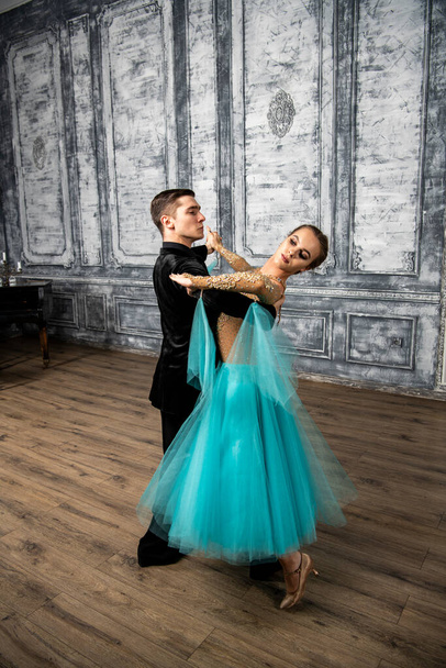 een jonge man in een zwart pak danst met een meisje in een turquoise jurk in de danszaal - Foto, afbeelding