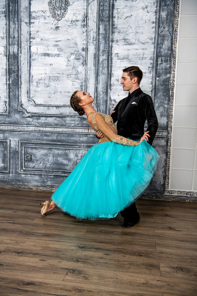 mladý muž v černém obleku tančí s dívkou v tyrkysových šatech v tanečním sále - Fotografie, Obrázek