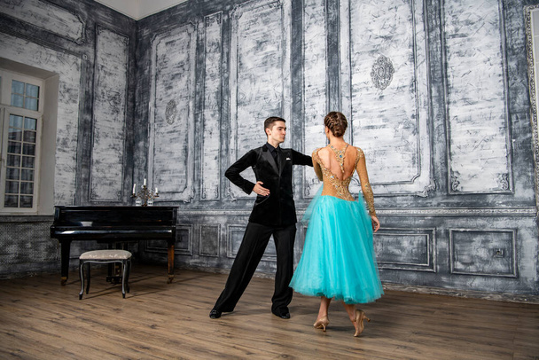 un joven con un traje negro está bailando con una chica en un vestido de turquesa en el salón de baile - Foto, Imagen