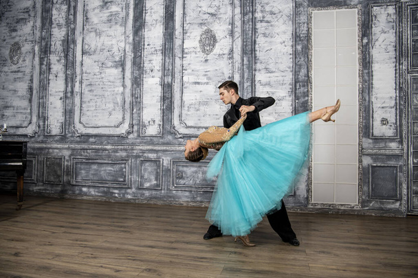 молодий чоловік в чорному костюмі танцює з дівчиною в бірюзовій сукні в танцювальному залі
 - Фото, зображення