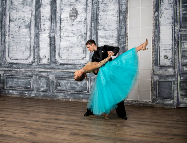 un joven con un traje negro está bailando con una chica en un vestido de turquesa en el salón de baile - Foto, imagen