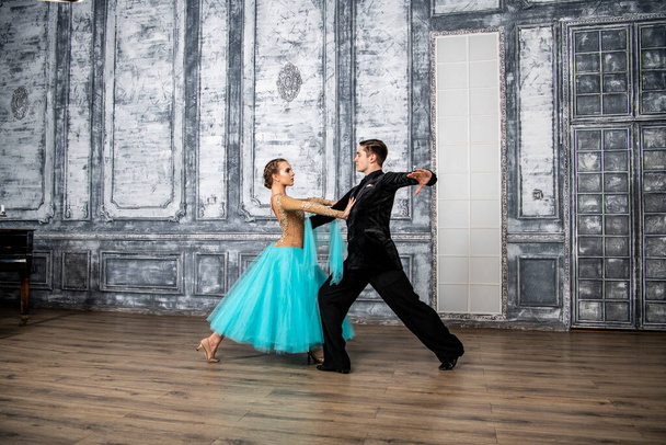 młody mężczyzna w czarnym garniturze tańczy z dziewczyną w turkusowej sukience w sali tanecznej - Zdjęcie, obraz