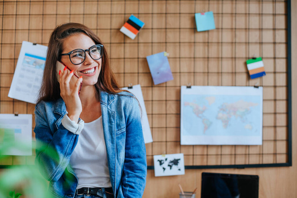 Szczęśliwa kobieta biznesu w okularach rozmawia z telefonem komórkowym w nowoczesnym biurze. - Zdjęcie, obraz