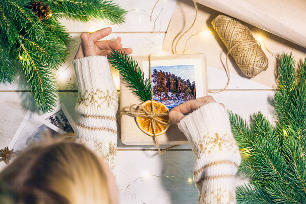 女性の手は、環境に優しいスタイルで山の写真でボックスクリスマスギフトを保持:自然のラフ紙、ジュートのロープ、トウヒ小枝、ヴィンテージはさみ。贈り物としての旅行. - 写真・画像