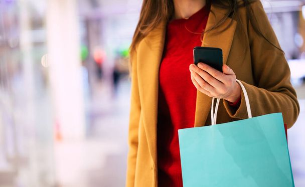 Close up photo of female hands with shopping bag and smart phone in the mall while buying some clothes - Foto, afbeelding