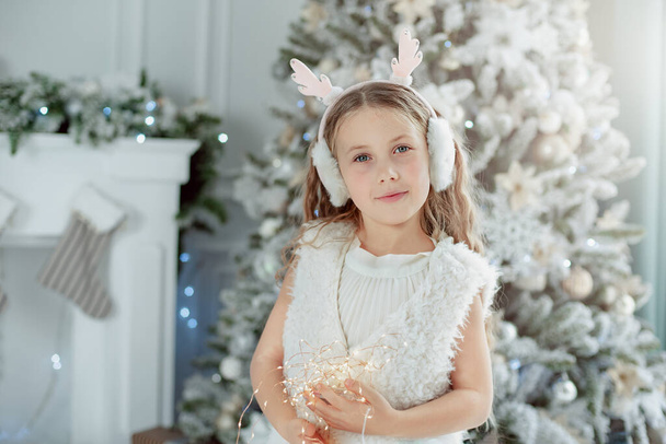 little girl under Christmas tree. Cute Christmas Child in white dress. Holiday season. New Year - Фото, изображение