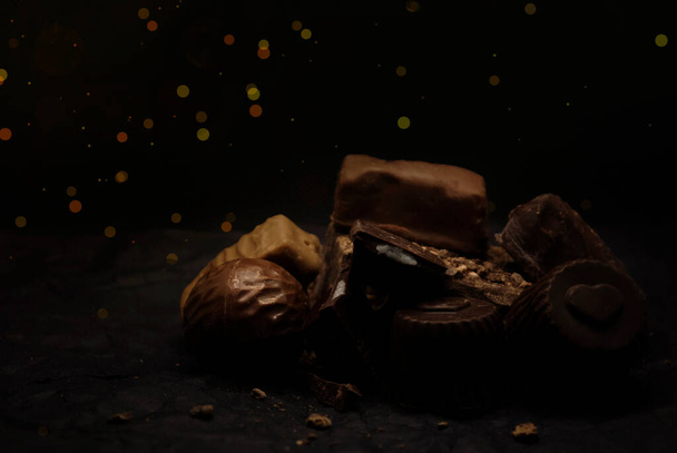 Divers bonbons sur fond noir, bokeh, paillettes. Pyramide de chocolats. Lieu pour le texte, logo. - Photo, image