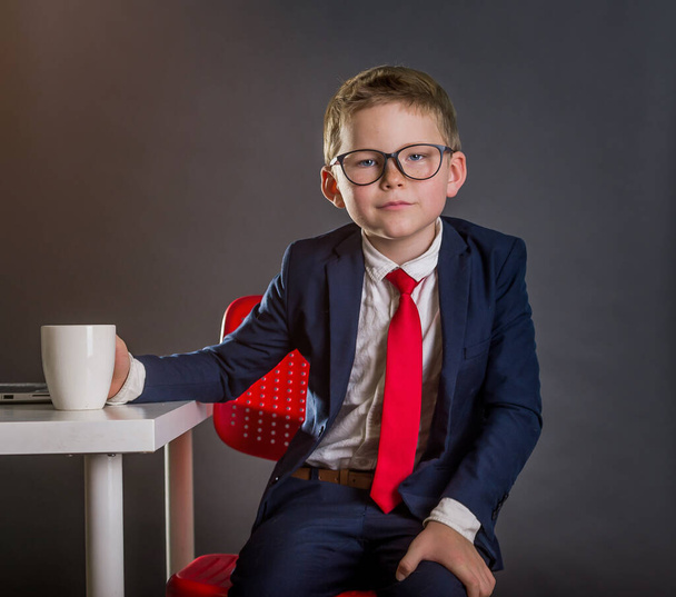 Little businessman in the office. Child in suit, red necktie and glasses. Fashion kid in elegant suit studying in business school. - Foto, imagen