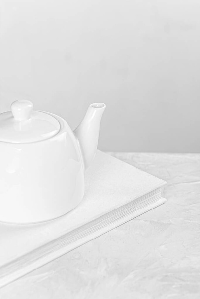 White ceramic kettle stands on white book - Foto, Imagem