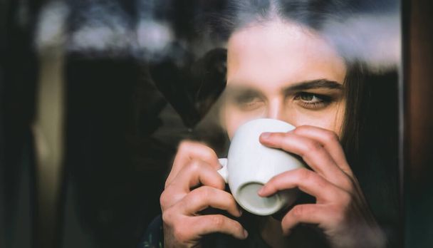 зимние каникулы, горячие напитки и люди концепции. красивая женщина пьет кофе за окном. крашеное сердце на туманном стекле. - Фото, изображение