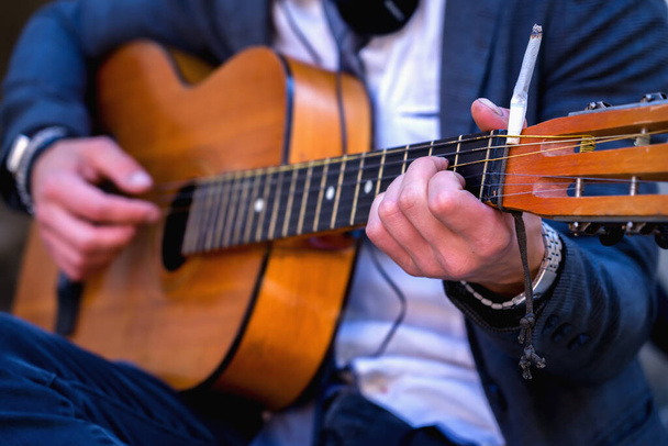 Μουσική του δρόμου. Άντρας μουσικός παίζει κιθάρα σε εξωτερικούς χώρους στο δρόμο της παλιάς ευρωπαϊκής πόλης. Κάψιμο από τσιγάρο στο κεφάλι. Επιλεκτική εστίαση. - Φωτογραφία, εικόνα