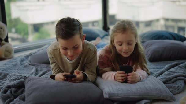 Knifflige Kinder süchtig nach Handyspielen. Geschwister spielen zu Hause auf Smartphones. - Filmmaterial, Video
