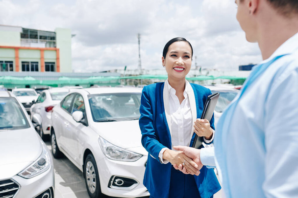 Smiling pretty Vietnamese car dealership saleswoman in suit shaking hand of customer - Photo, Image