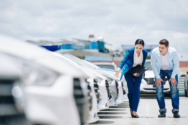 Női autókereskedés menedzser bemutató új járművek férfi ügyfél, és segít neki, hogy válasszon egyet - Fotó, kép