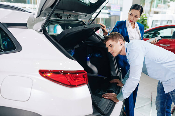 Handsome young man looking inside car trunk in dealership - Photo, Image