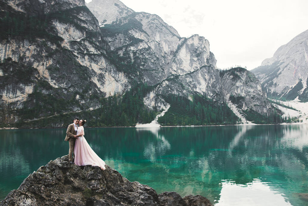 Romantic wedding moment, couple of newlyweds smiling portrait, bride and groom hugging near a beautiful lake in the mountains - 写真・画像