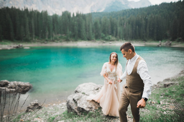 Young couple near lake Karersee, Italy. Holding hands at the stone at lake - Foto, afbeelding