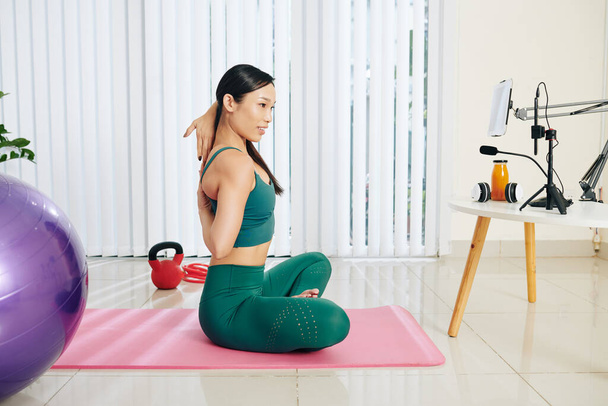 Fit junge Frau, die sich beim Online-Yoga mit den Fingern beider Hände hinter dem Rücken festhält - Foto, Bild