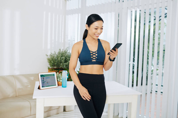 Smiling pretty Vietnamese fitness blogger checking comments and messages on her social media platforms - Φωτογραφία, εικόνα