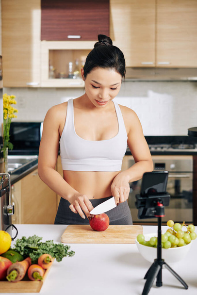 Melko ohut nuori aasialainen nainen tekee videon itsestään leikkaamalla hedelmiä terveelliseksi aamiaiseksi - Valokuva, kuva