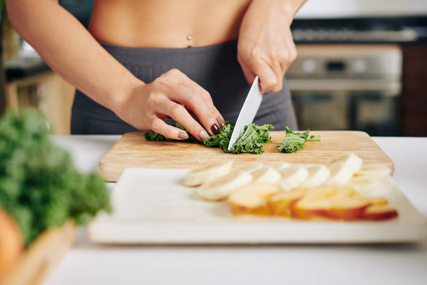 Close-up image of fit young woman cutting kale leaves and making smoothie - Zdjęcie, obraz