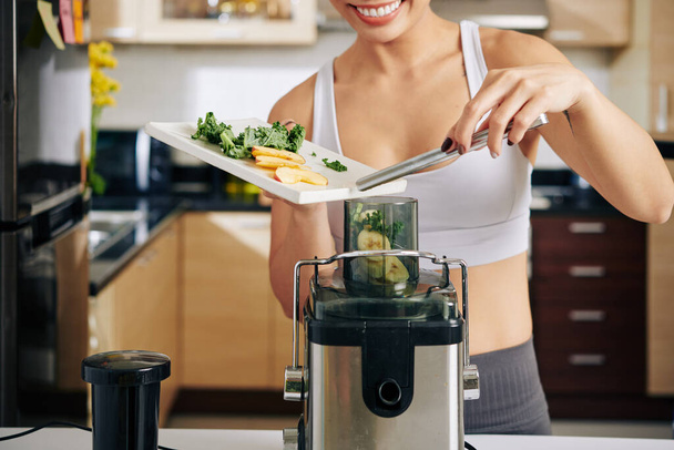 Close-up image of woman putting kale leaves, banana and apple pieces in juicer - Photo, Image