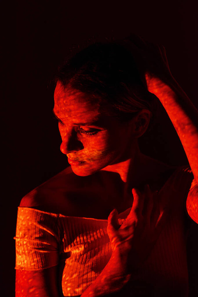 Творческий портрет женщины, освещаемой цветными огнями на темном фоне. - Фото, изображение