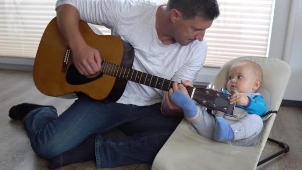 Un padre cariñoso toca la guitarra con su adorable bebé en un columpio de bebé 4K - Metraje, vídeo