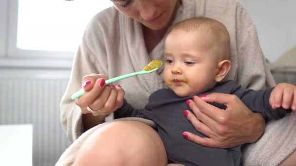 Een schattige baby jongen eten gemengde groene groenten met mama houden de lepel 4K - Video