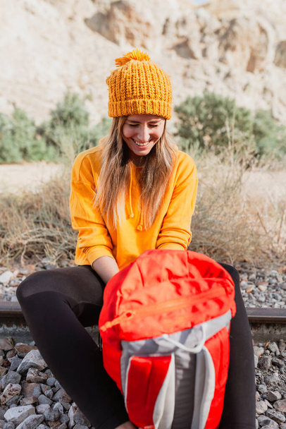 Femme trekking repose sur une voie ferrée abandonnée à la recherche de quelque chose dans son sac à dos - Photo, image