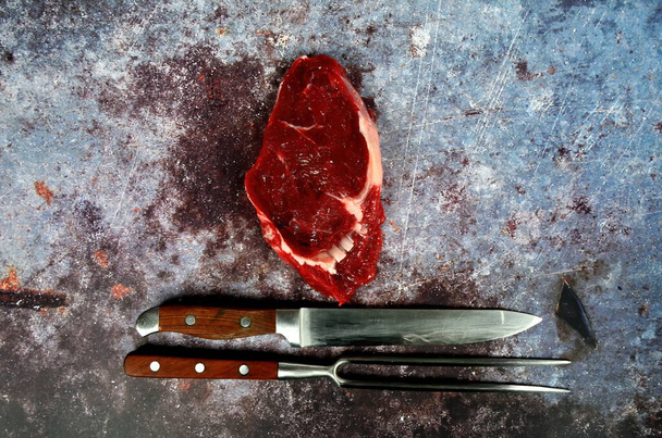Carne cruda con cuchillo para asar y tenedor, filete de res sobre fondo rústico oscuro, vista superior, espacio para copiar - Foto, Imagen