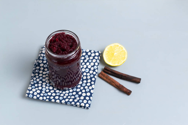 Natural beet jam in a glass jar with lemon and cinnamon on a blue napkin on a gray background. Vegetarianism concept. Copy space. Selective focus. - Photo, Image