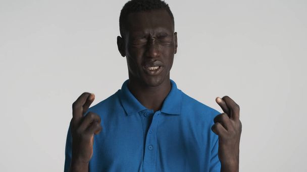 Emocional afro-americano cara com dedos cruzados esperança na boa sorte isolado no fundo branco. Expressão de oração - Foto, Imagem