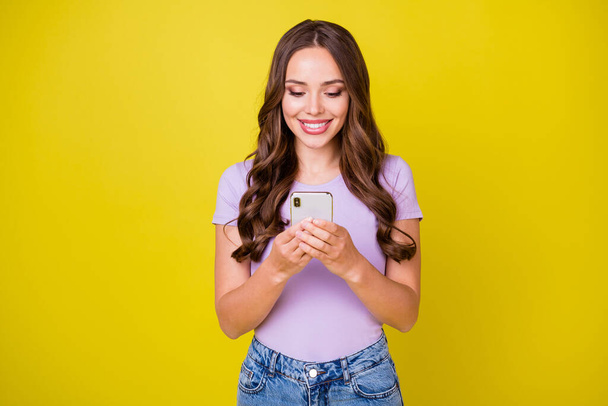 Portrait of attractive focused cheerful wavy-haired girl using gadget smm post isolated over vibrant yellow color background - Фото, зображення