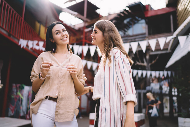 Pretty female fellows enjoying friendship relations and together vacations for exploring world standing at urbanity and discussing funny stories, cheerful women 20s socialising at city street - Foto, Imagem