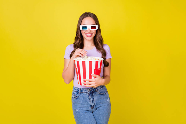 Portrait of attractive cheerful wavy-haired girl eating corn watching 3d film isolated bright yellow color background - Foto, Bild