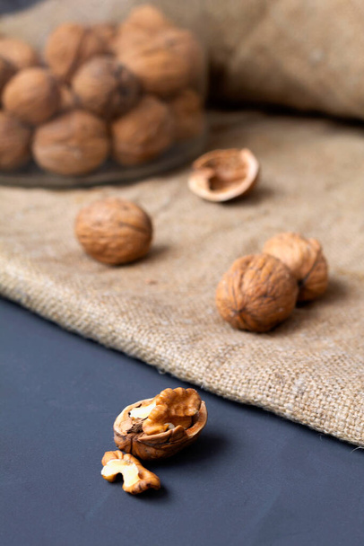 close-up walnuts. unpeeled and peeled walnuts in shells on a black table and in a glass jar. brown nuts with sackcloth on a dark background. copy space. dried walnut and fruit. vertical - Photo, Image