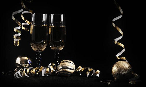 A glass of champagne. Golden serpentine. Christmas tree balls.Items on a black background. New year and Christmas greetings. Festive still life. - Foto, imagen