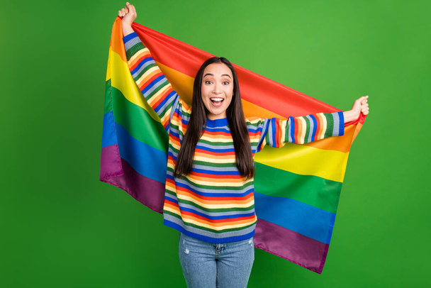 Portrait of attractive excited cheerful girl holding in hands lgbt flag having fun isolated over bright green color background - Fotoğraf, Görsel