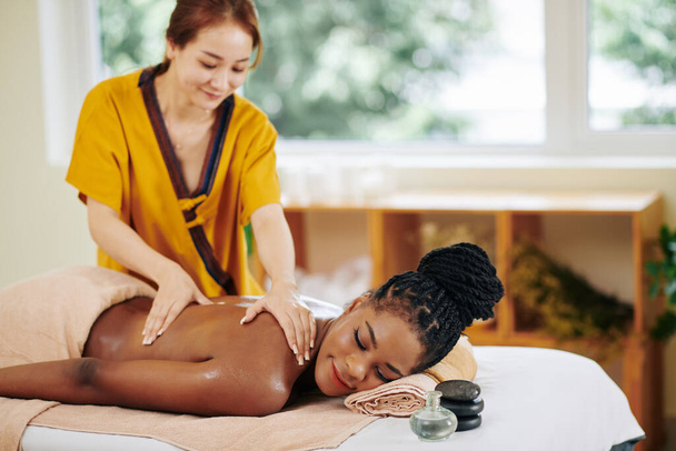 Lächelnde hübsche Afroamerikanerin bekommt Körpermassage im Wellness-Salon - Foto, Bild