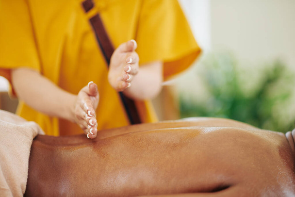 Masseuse faisant mouvement de piratage lors du massage dos de la cliente avec des huiles - Photo, image