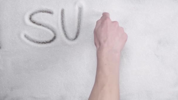 Man hand schrijft het woord suiker doodt op een achtergrond van witte suiker. - Video