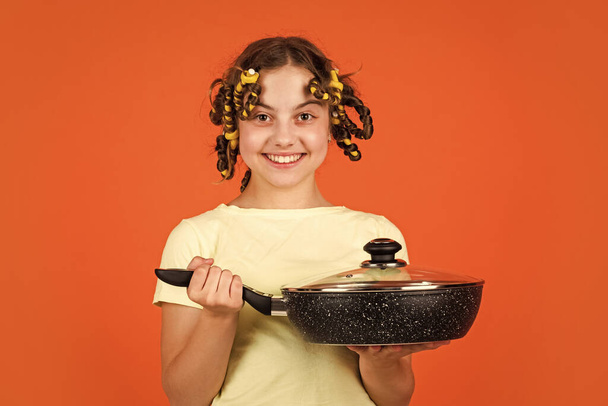 Stereotype housewife style. Small girl with curlers in hair. Pin up style. Girl hold Frying Pan. Little kid hold pan cooking meal. Shop home utensils. Kitchen accessories. Culinary and house duties - Fotografie, Obrázek