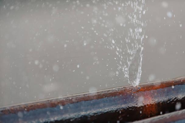Salpicaduras de agua de un agujero en una tubería de agua de metal. - Foto, Imagen