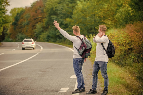 Try to stop some car. Reason people pick up hitchhikers. Missed their bus. Need help. Cheap transport. Transport problem. Travel and transport concept. Twins men at edge of road nature background - Photo, image