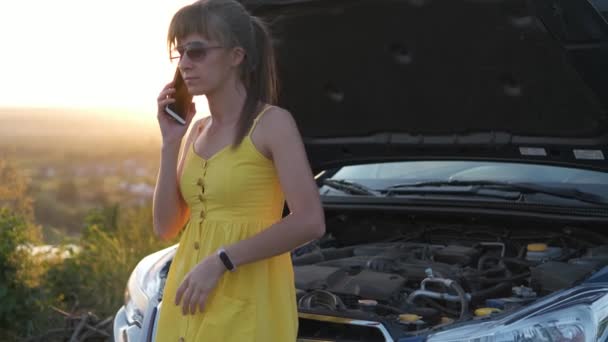 gespannen vrouw bestuurder praten op een telefoon staan in de buurt van haar voertuig met popped kap met motorproblemen. - Video